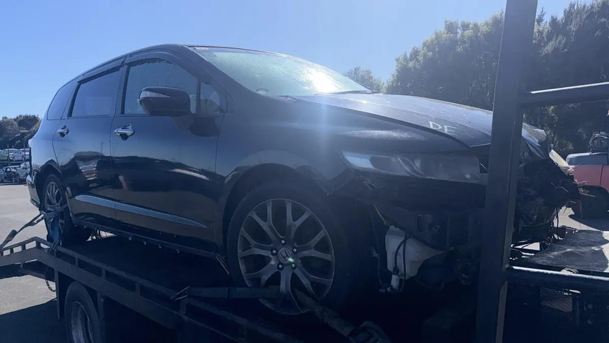 Black Honda Odyssey people mover with front crash damage loaded on a tow truck for removal