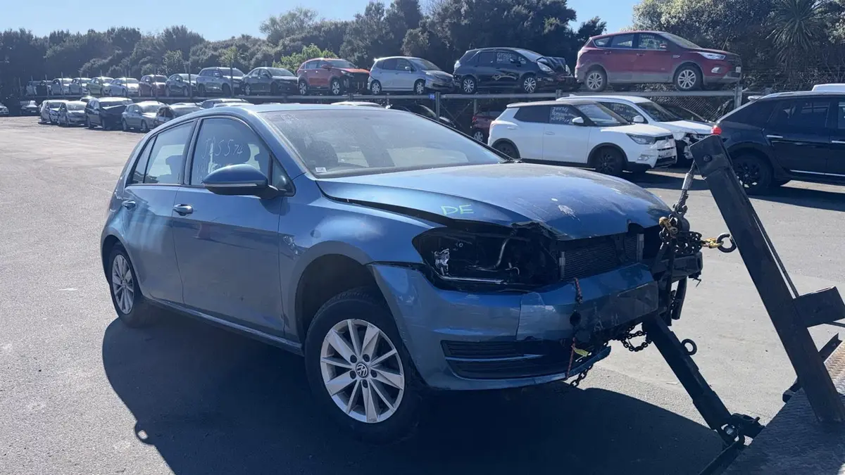 Blue Volkswagen Golf with heavy front-end accident damage being towed for cash for cars